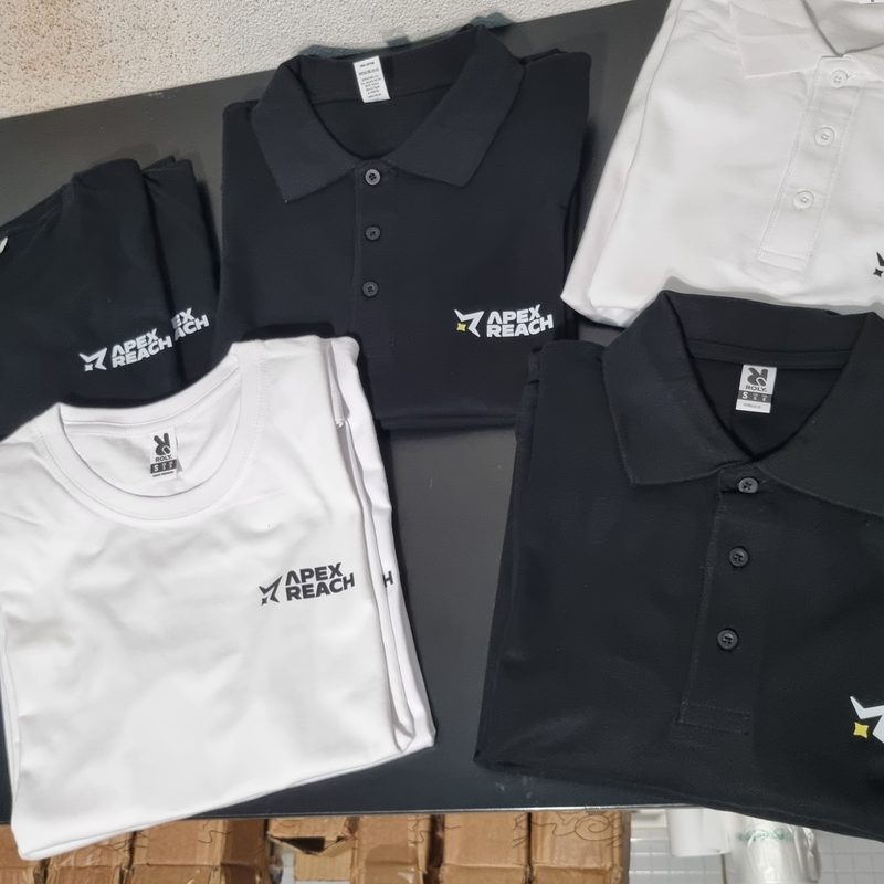 Encomenda de polos e t-shirts Apex Reach empilhados na oficina, prontos a entregar