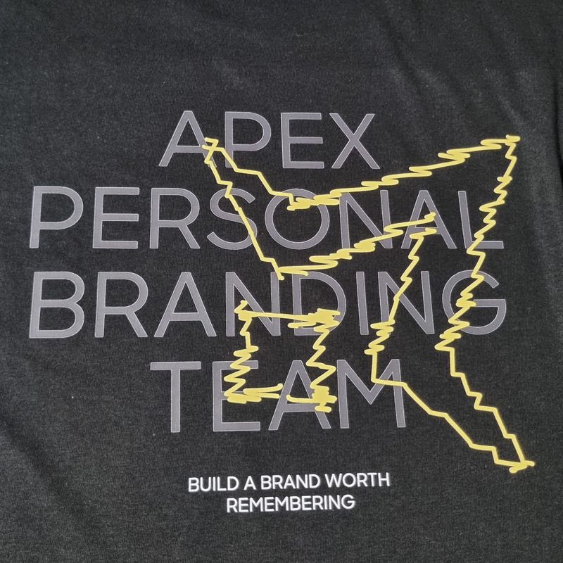 Costas de t-shirt preta com o lettering Apex Personal Branding Team estampado a cinzento e amarelo