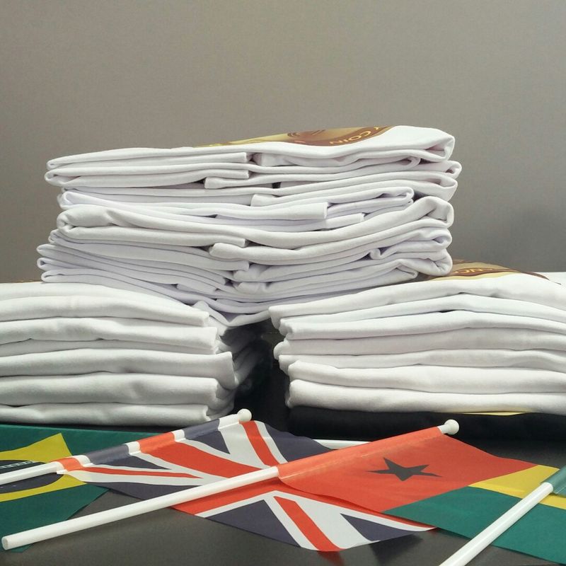 Pilhas de t-shirts brancas personalizadas para um evento internacional, com bandeiras de vários países